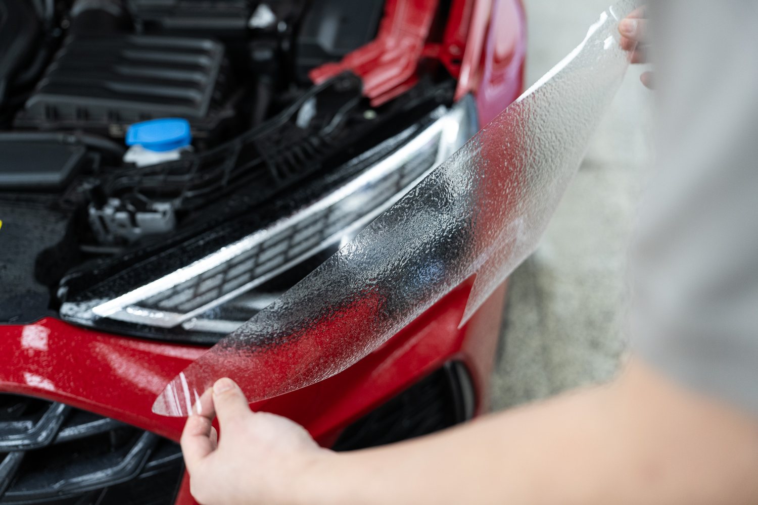 Headlight protection film being fitted to a red Audi
