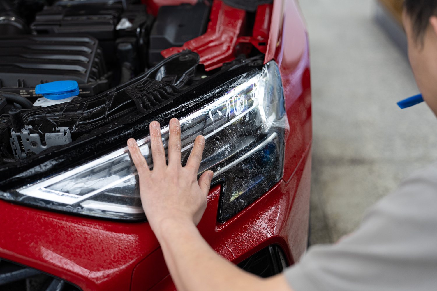 Headlight protection film being fitted to a red Audi