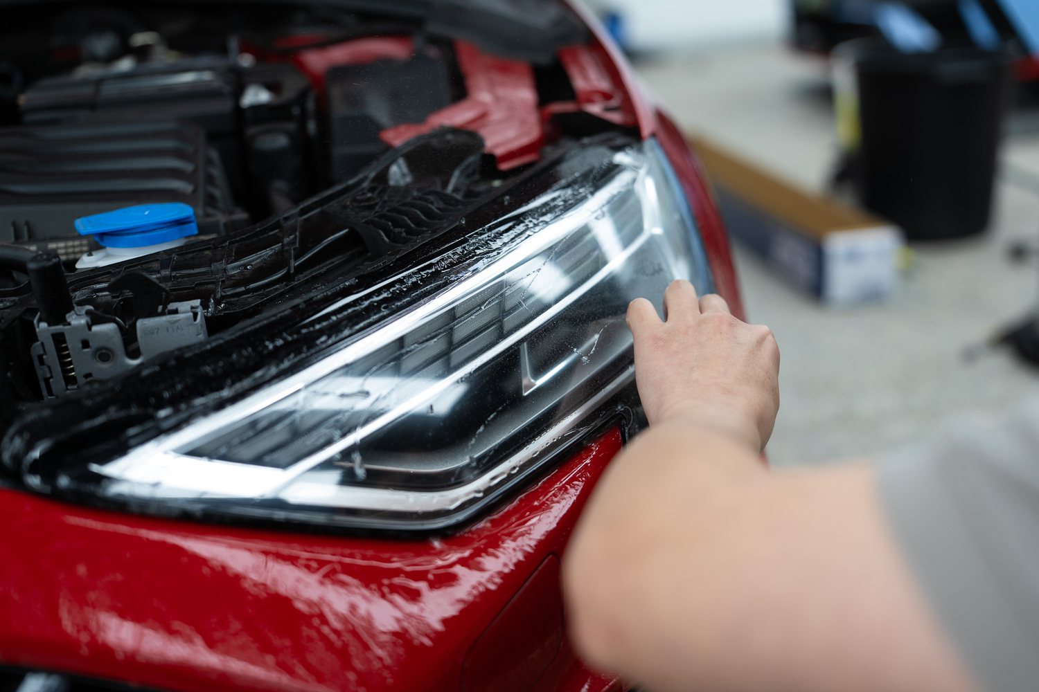 Headlight protection film being fitted to a red Audi