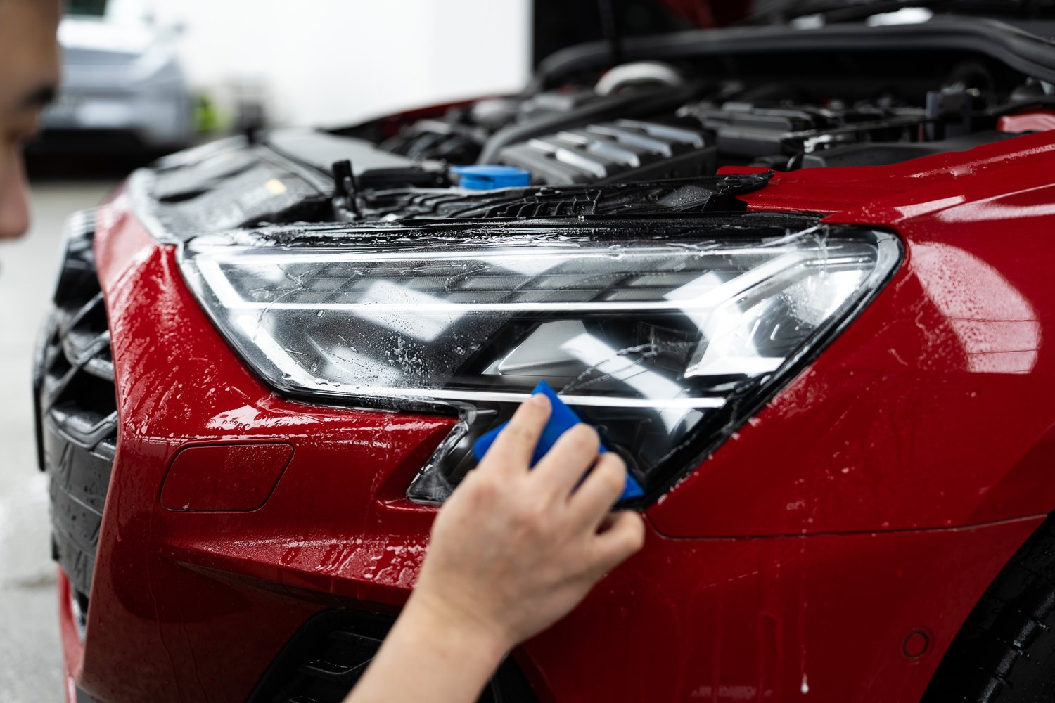 Headlight protection film being fitted to a red Audi