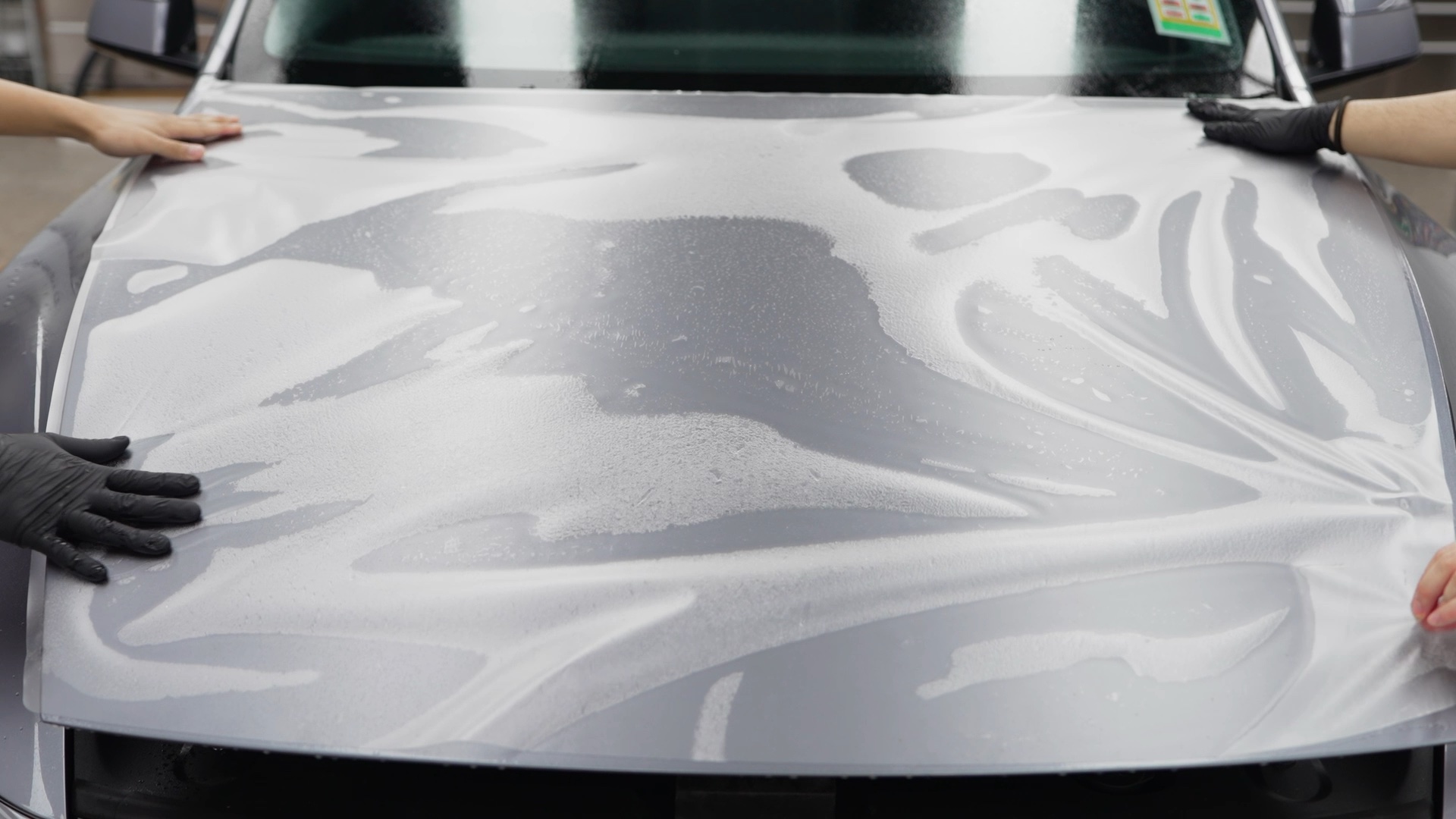 Two technicians laying paint protection film across a bonnet
