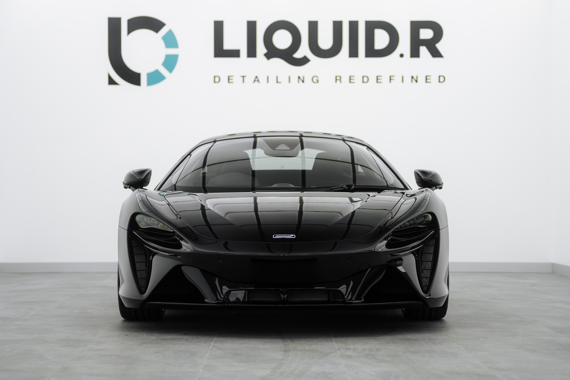 Black McLaren in front of the Liquid R logo wall