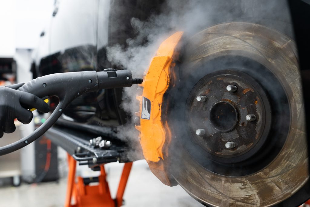 Steam cleaning an orange brake caliper during detailing