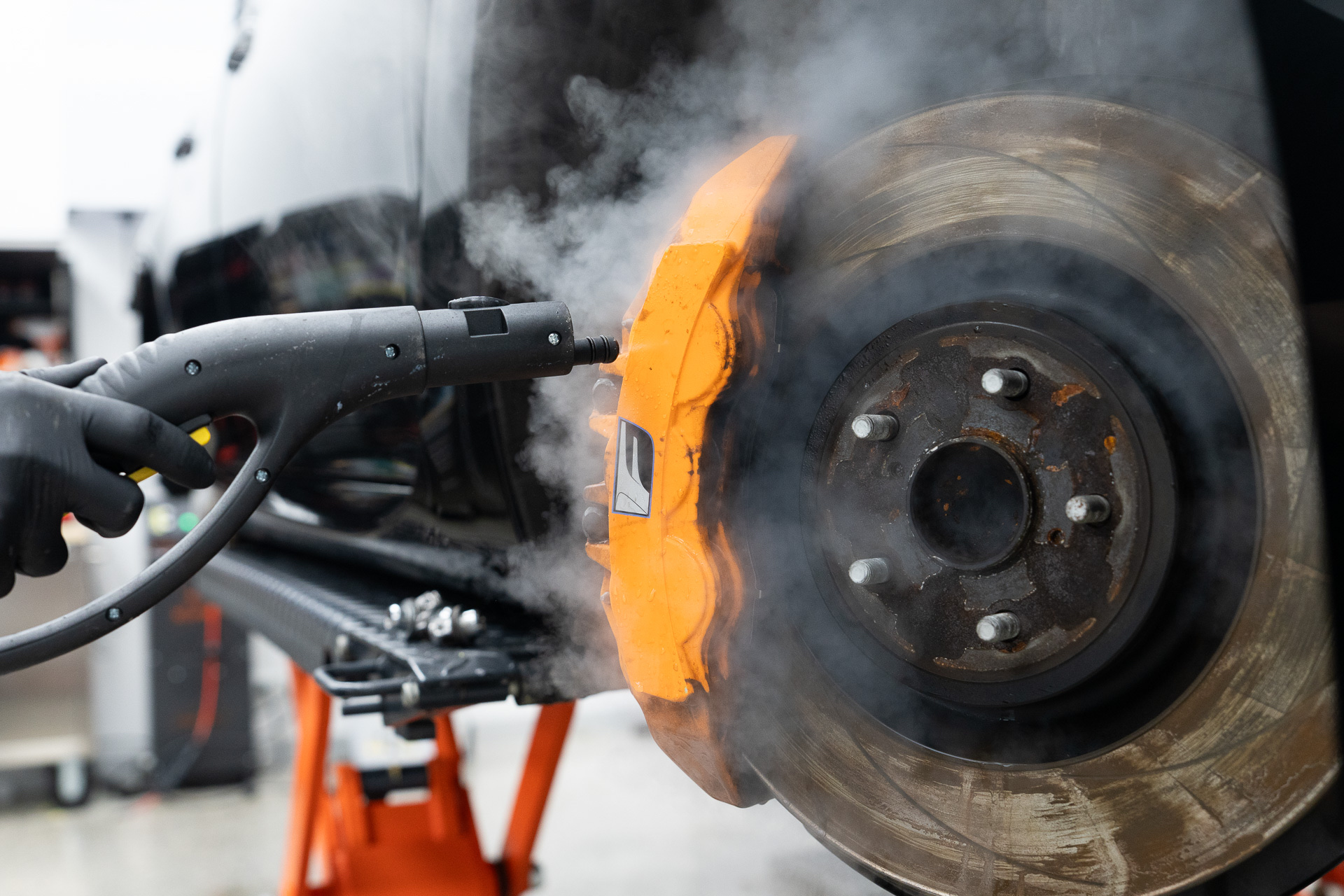 Steam cleaning an orange brake caliper during detailing