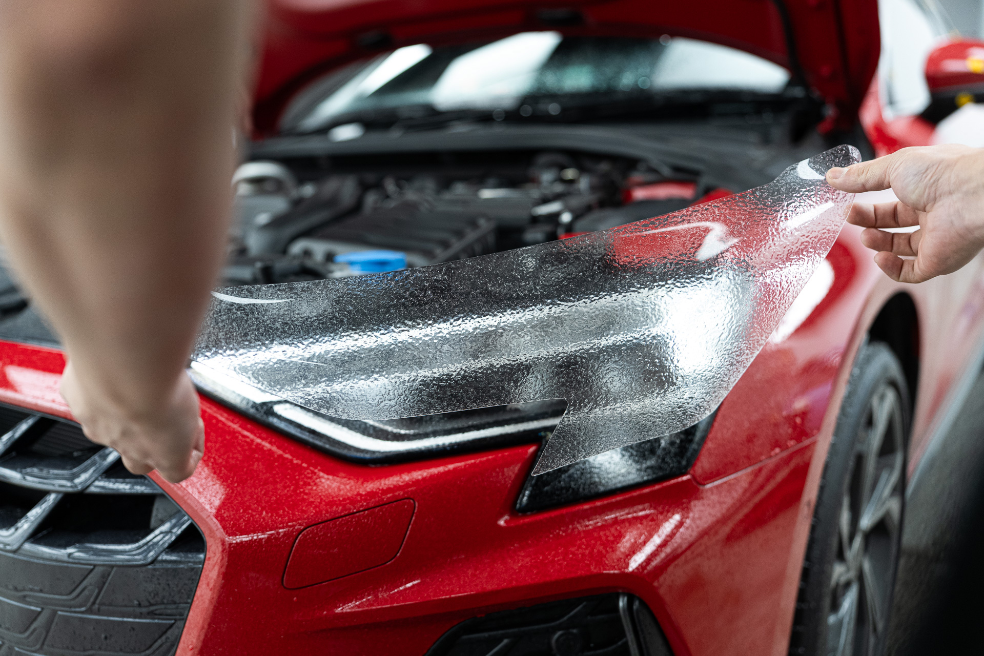 Headlight protection film being applied to a red car
