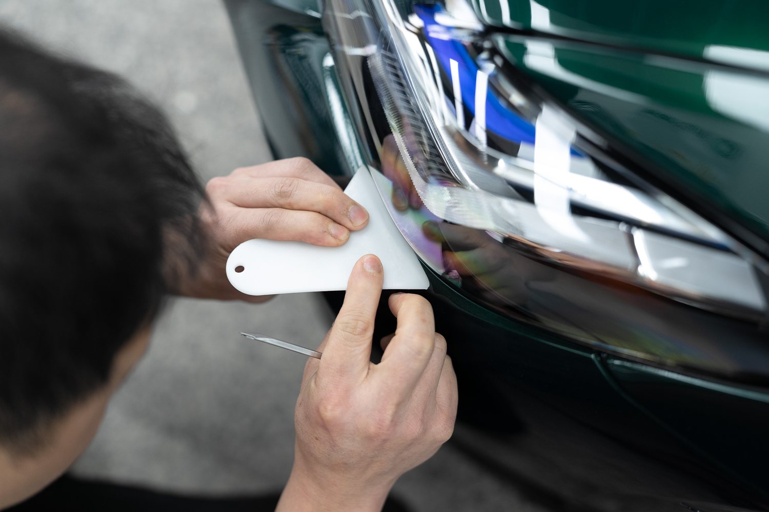 Squeegee fitting paint protection film around a headlight