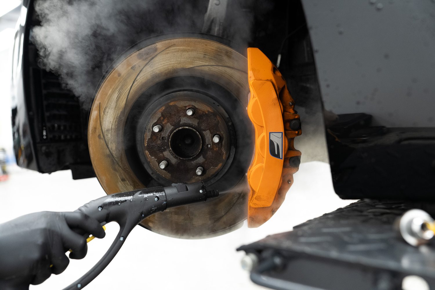 Steam cleaning an orange brake caliper