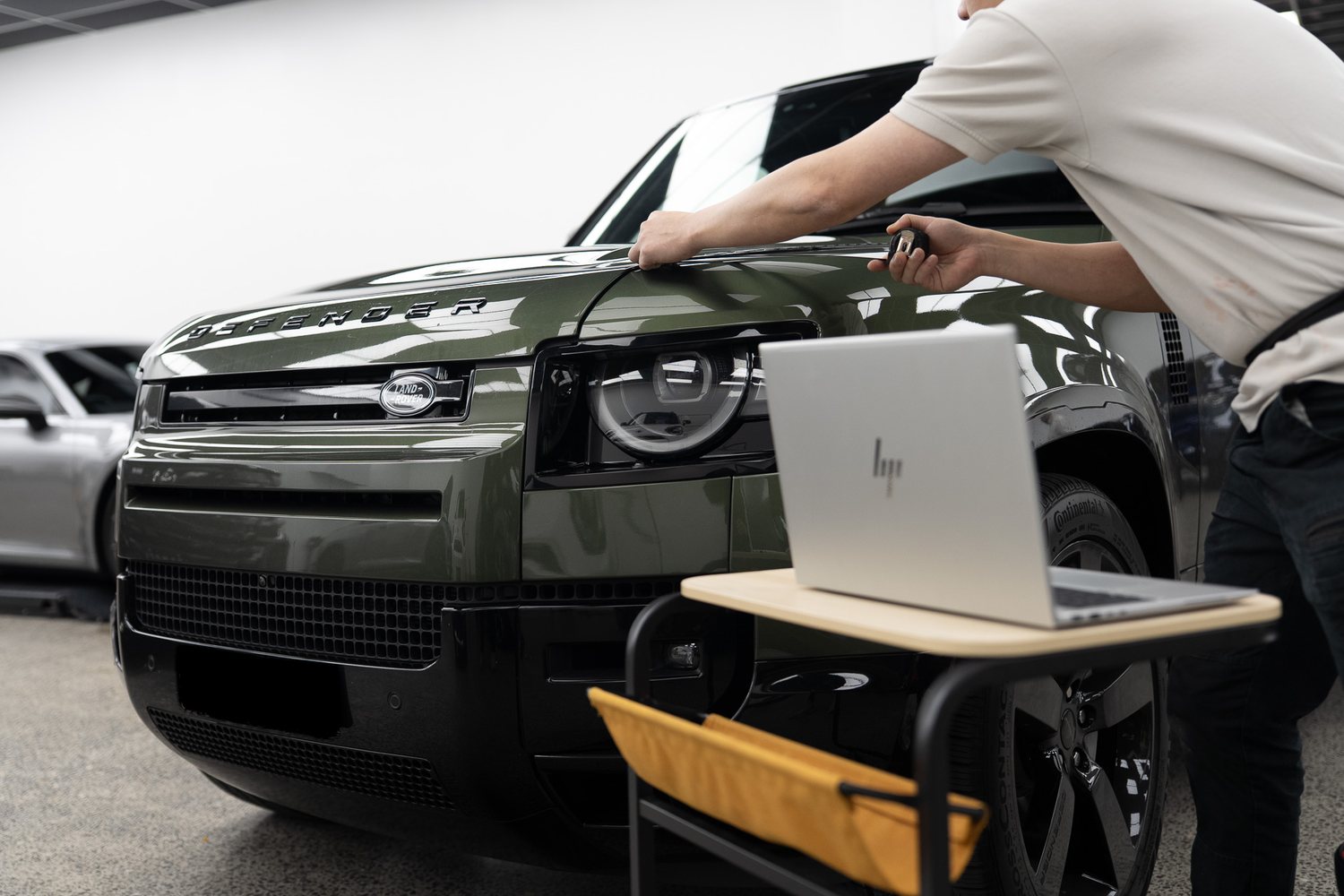 Technician checking a film pattern on a laptop beside a Land Rover Defender