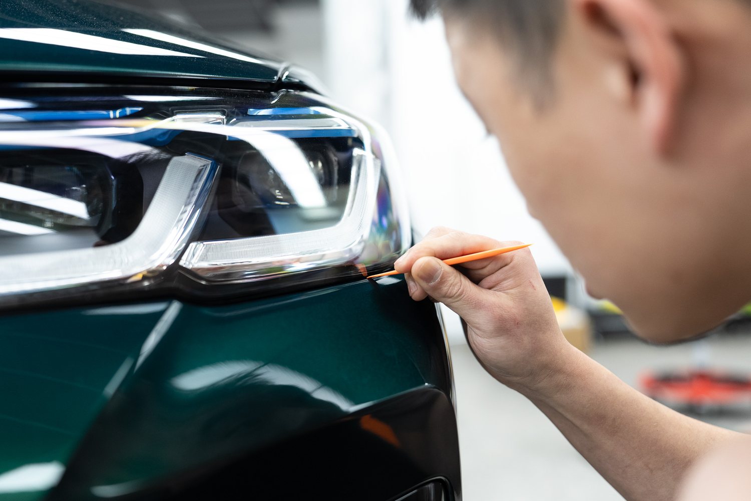 Technician trimming paint protection film beside a headlight